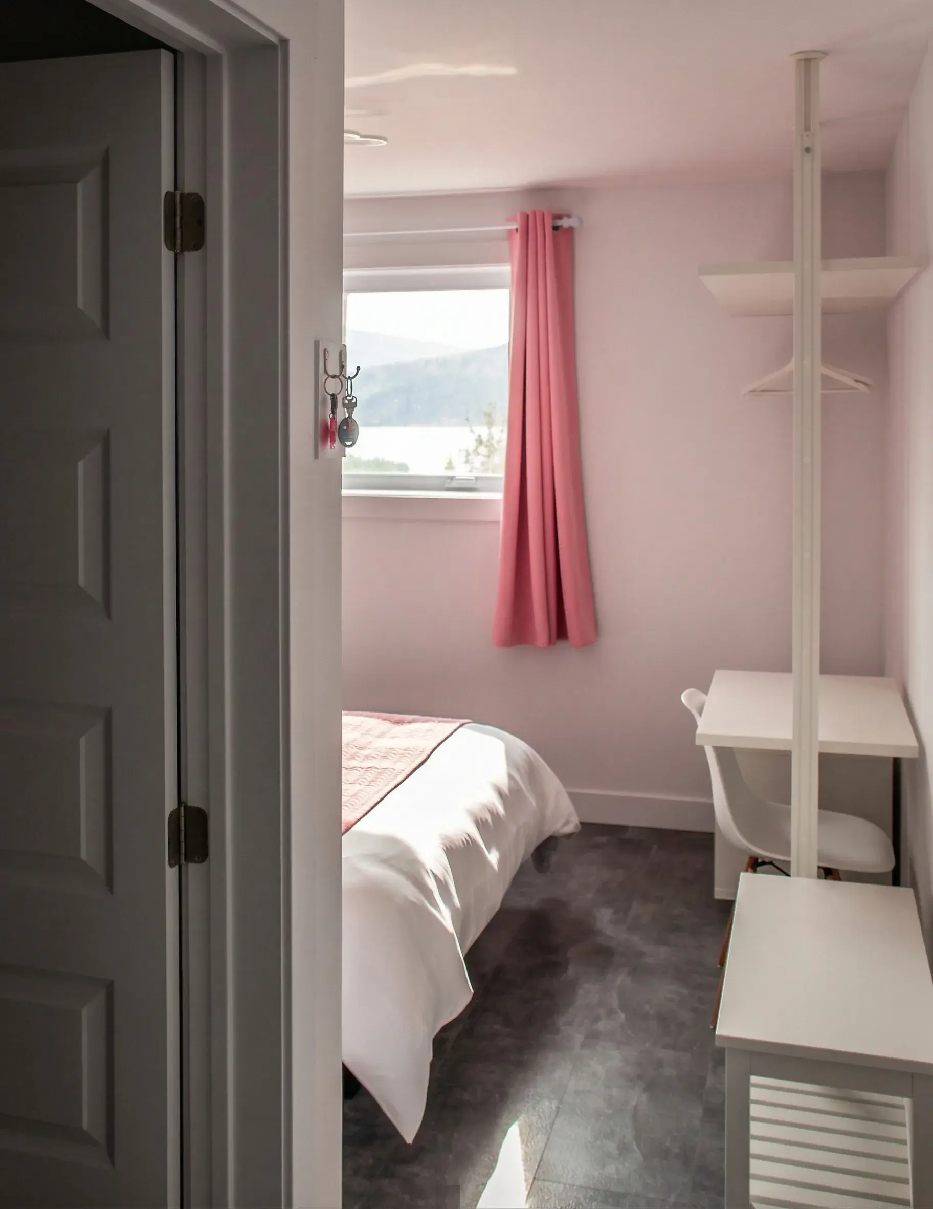 Chambre aux rideaux roses avec lit, bureau et vue sur les montagnes