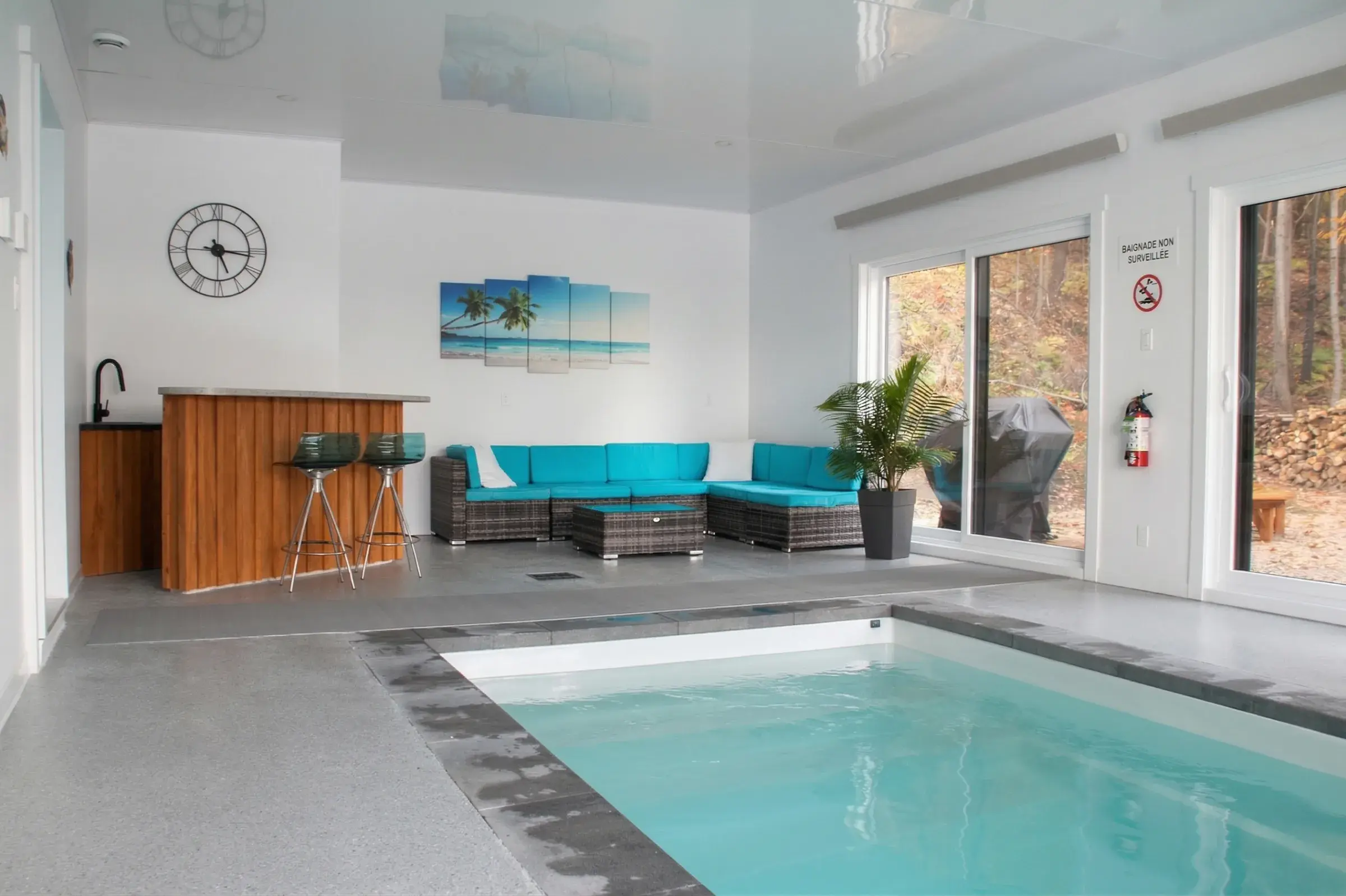 Piscine intérieure avec coin bar, canapé turquoise et baies sur la forêt