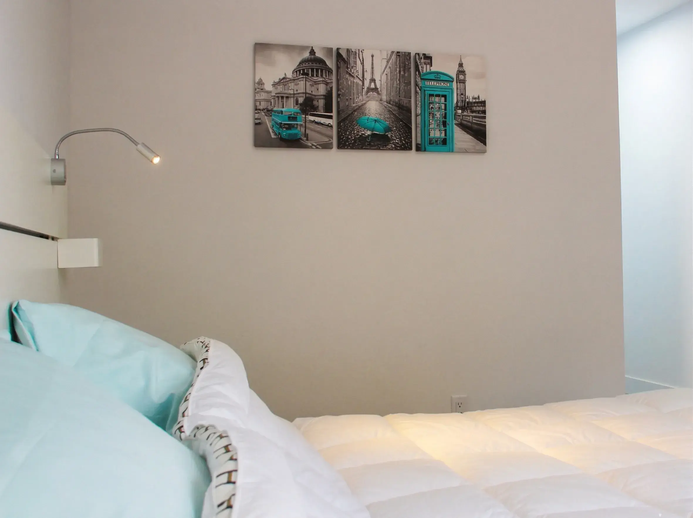 Chambre avec literie bleu turquoise et triptyque de villes au mur