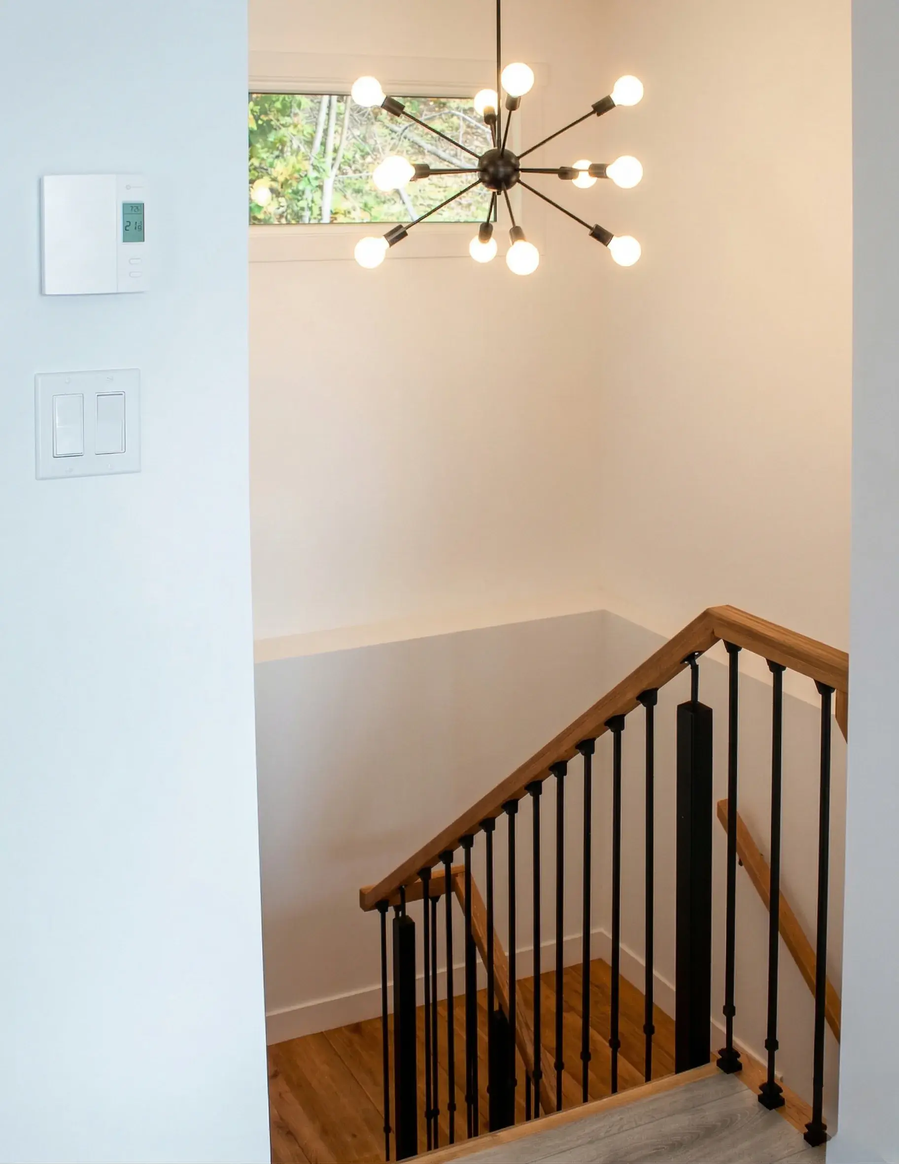 Palier d'étage avec lustre design et rampe d'escalier en bois