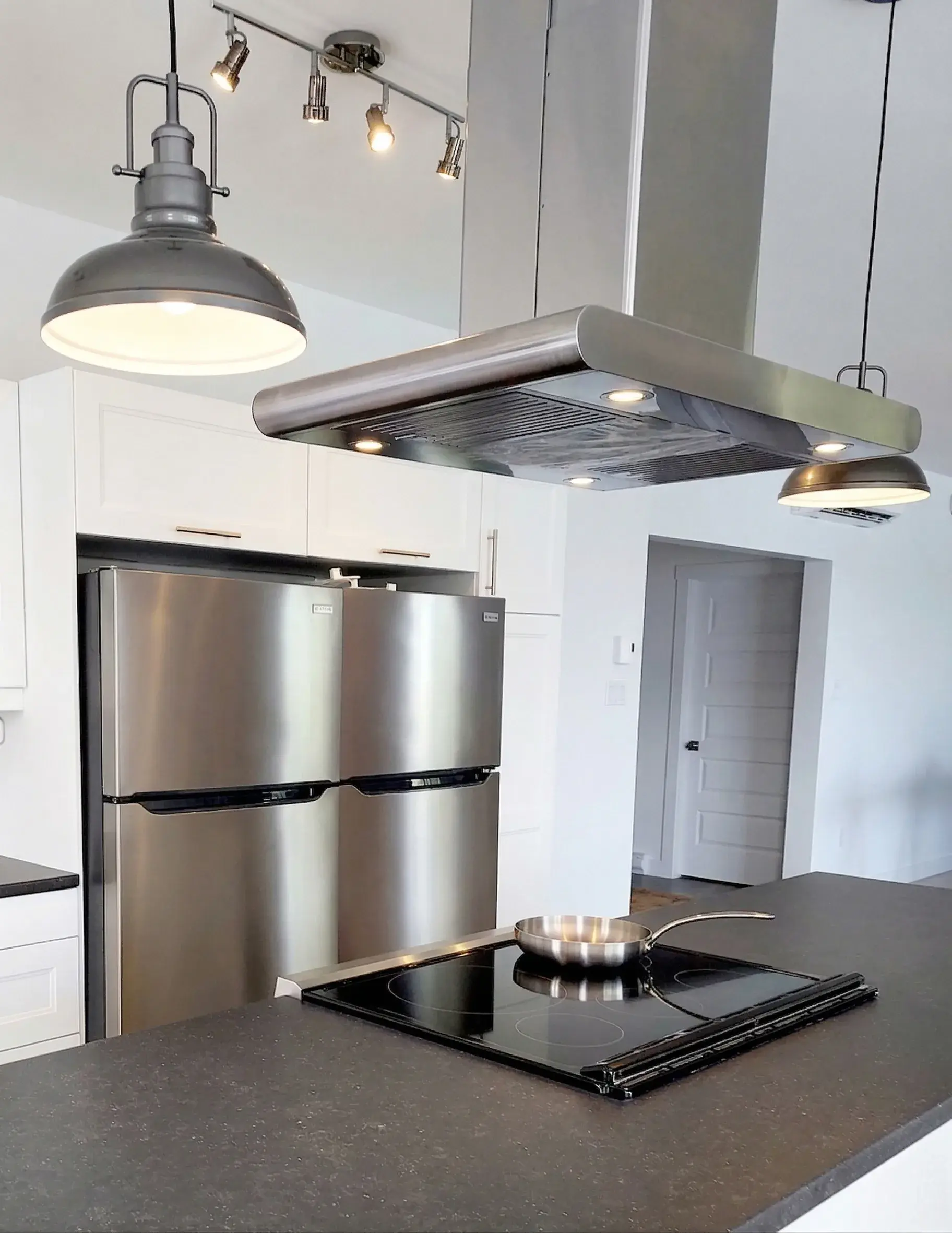 Plaque de cuisson sur l'îlot, réfrigérateur en inox et hotte suspendue