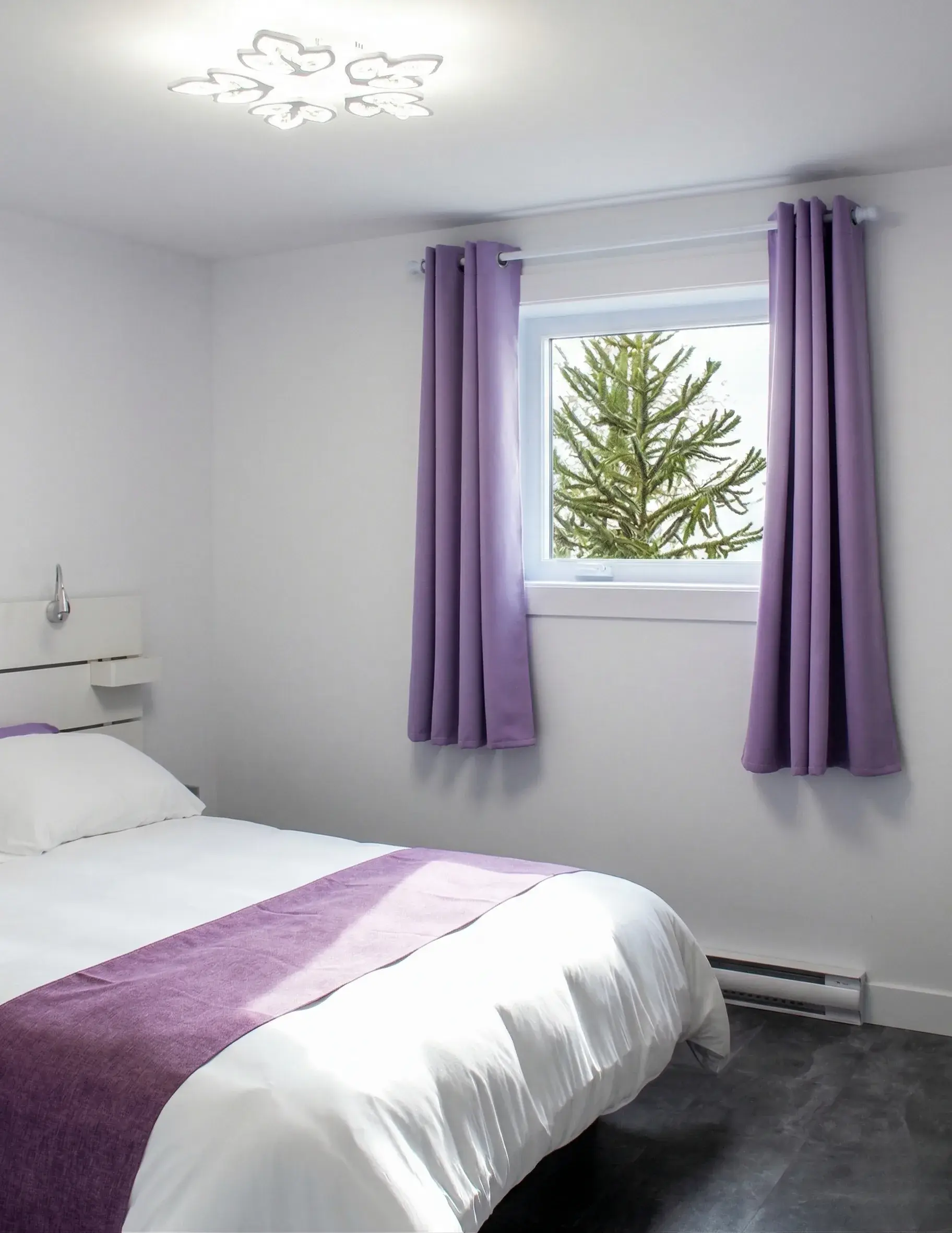 Chambre aux rideaux mauves avec lit double et vue sur un conifère