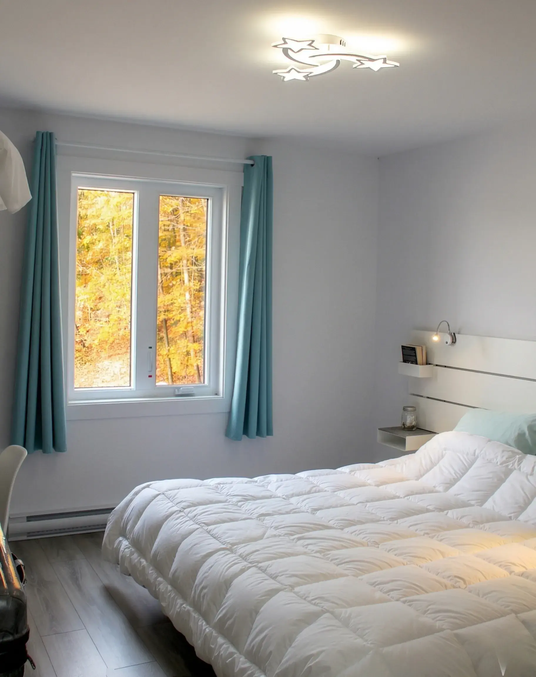 Chambre aux rideaux turquoise avec vue sur la forêt aux teintes d'automne